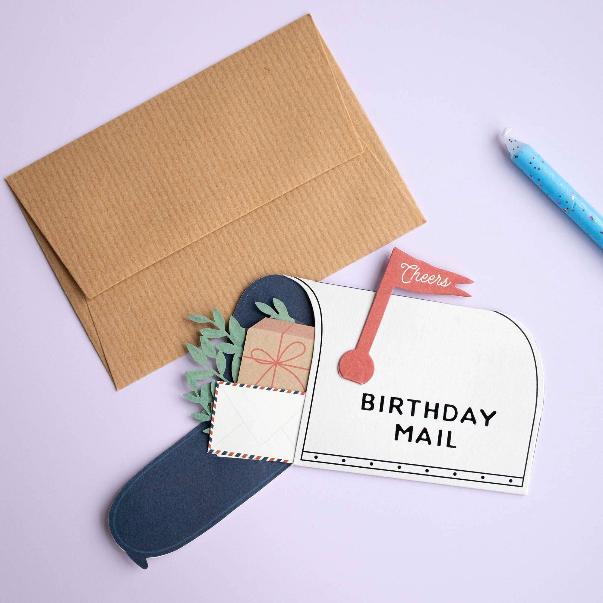 Birthday card with envelope and stationery items on a light purple background