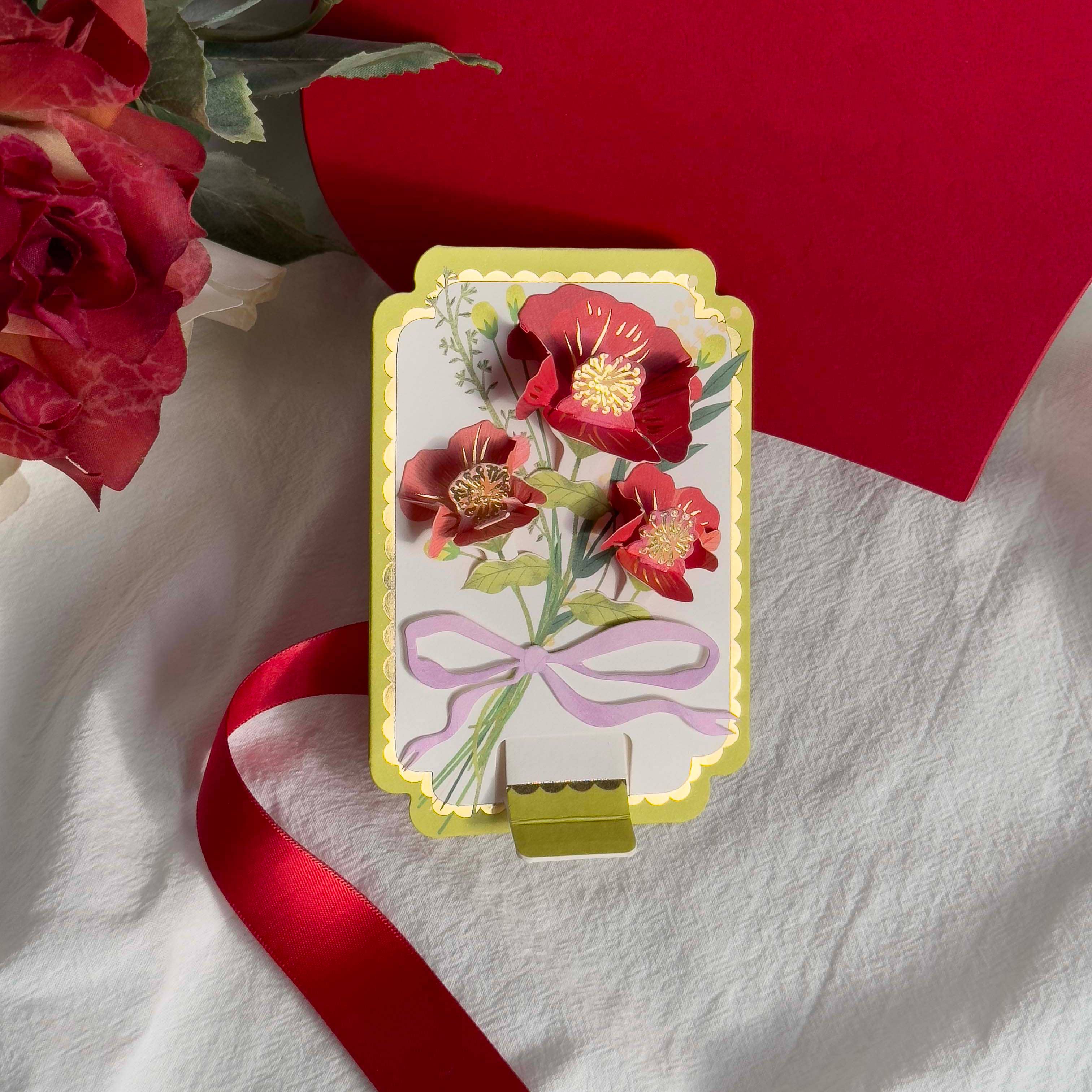 Decorative card with floral design and red ribbon on a white fabric background