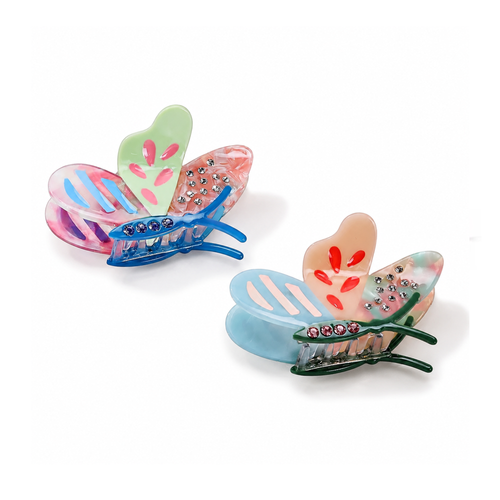 Two butterfly-shaped hair claw clips on a white background. One clip has pastel pink, blue, and green wings with rhinestone accents, and the other has light blue, peach, and green wings with rhinestone accents.
