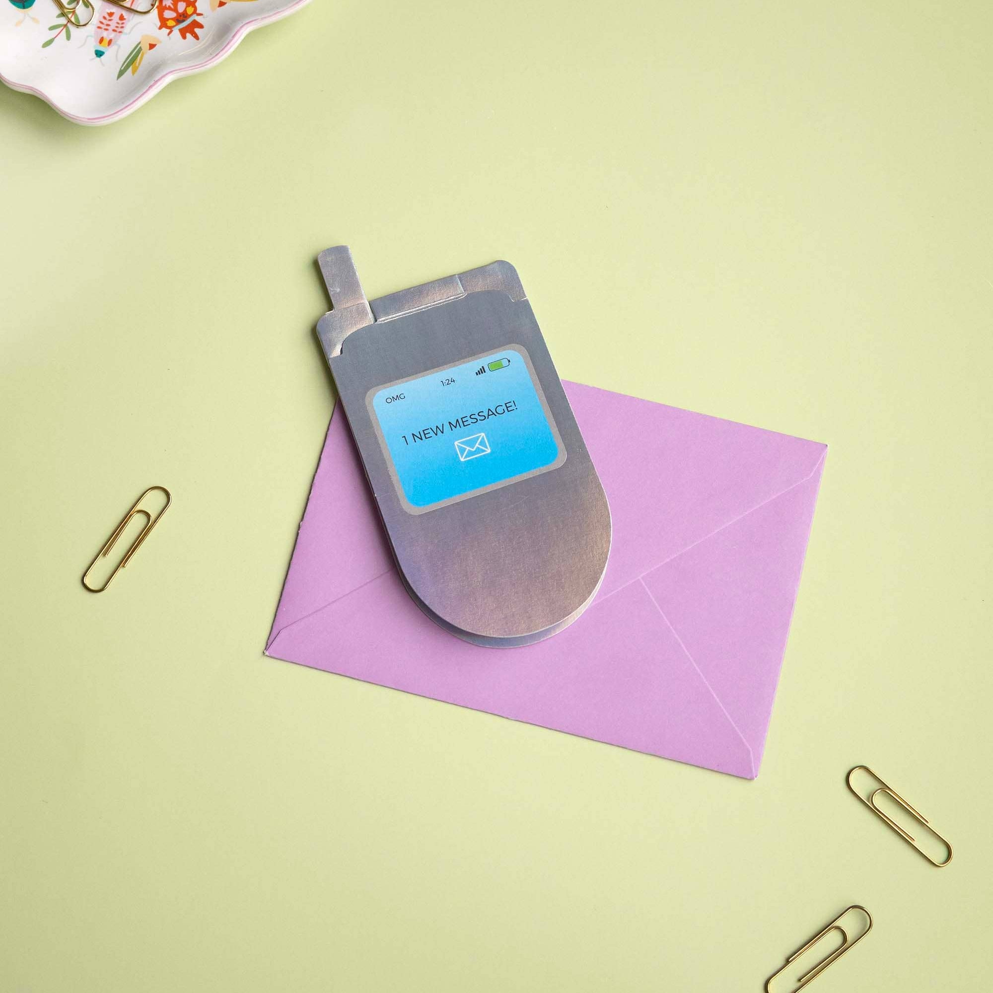 Vintage flip phone on a pink envelope with a light green background