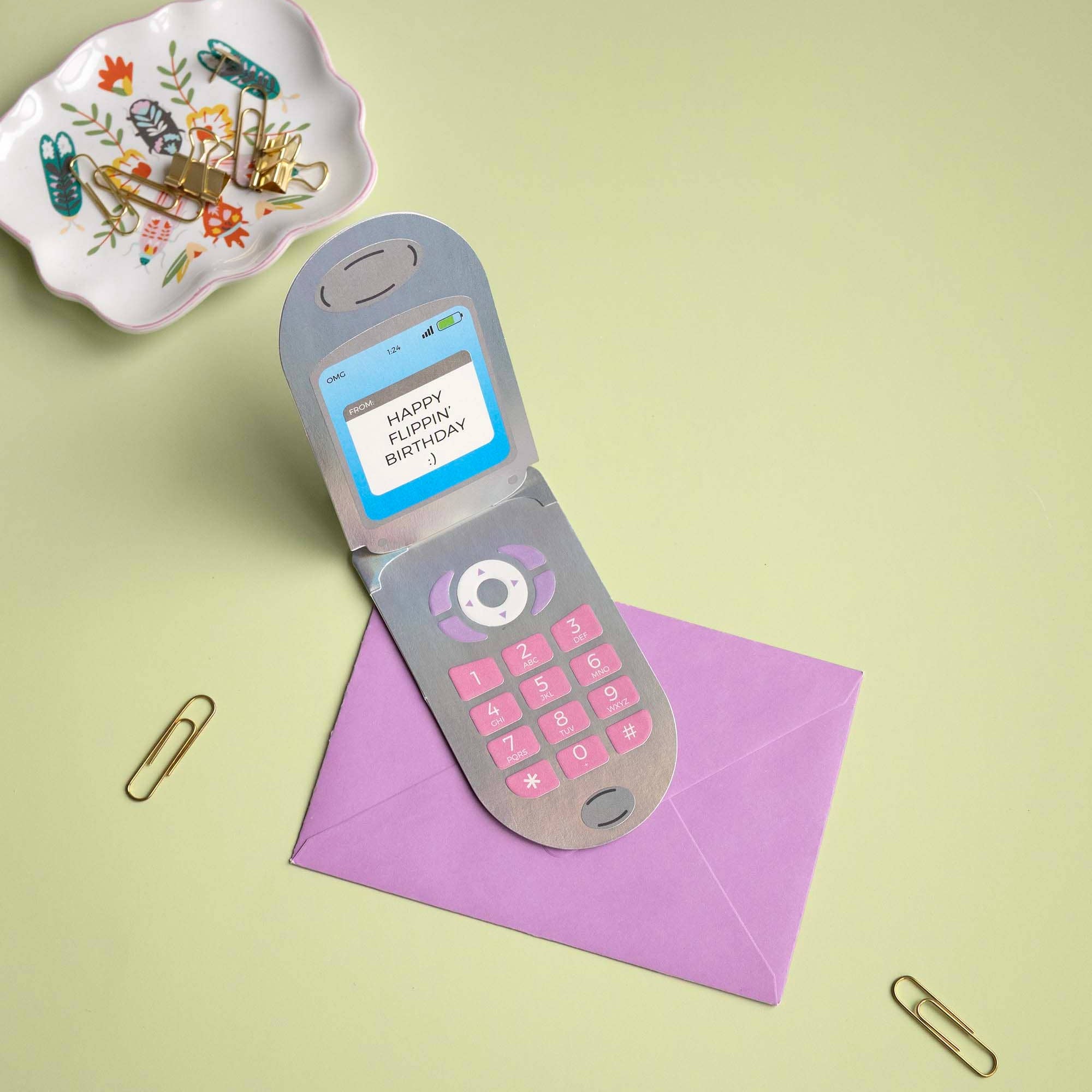 Toy phone with a screen and keypad on a purple envelope against a light green background